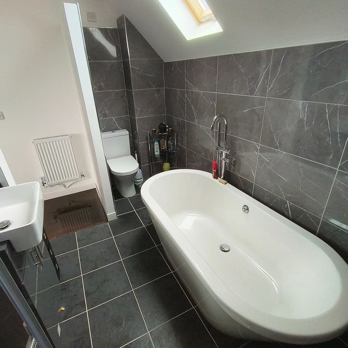 Bathroom with grey marble-effect wall and floor tiles around a freestanding bath