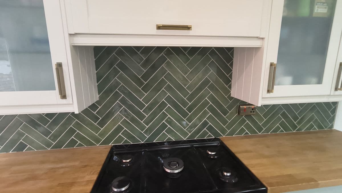 Green herringbone tile splashback above a kitchen gas hob
